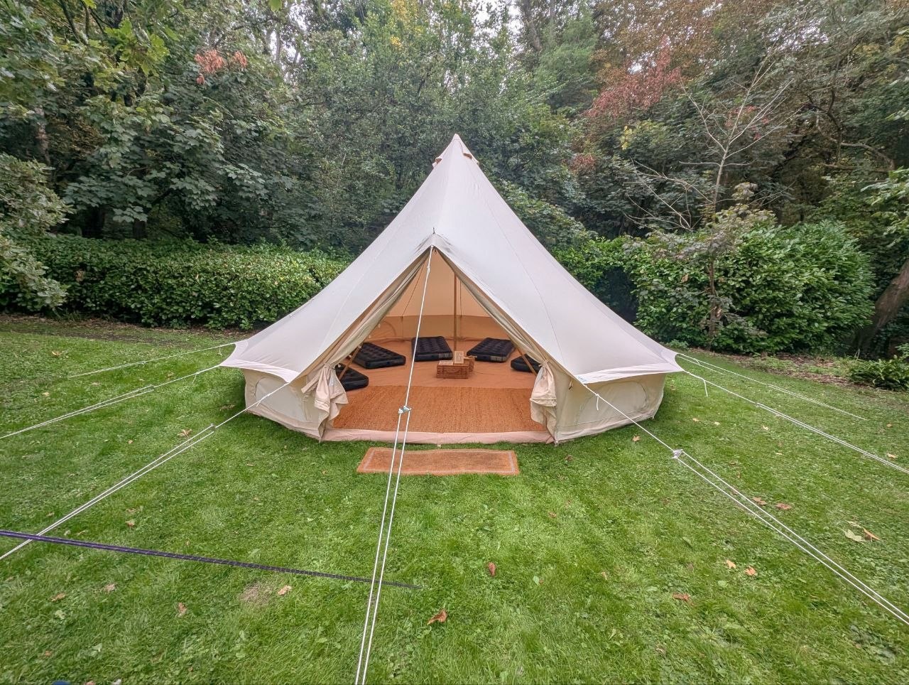 Open bell tent on a garden lawn, showing the entrance and surrounding guy ropes