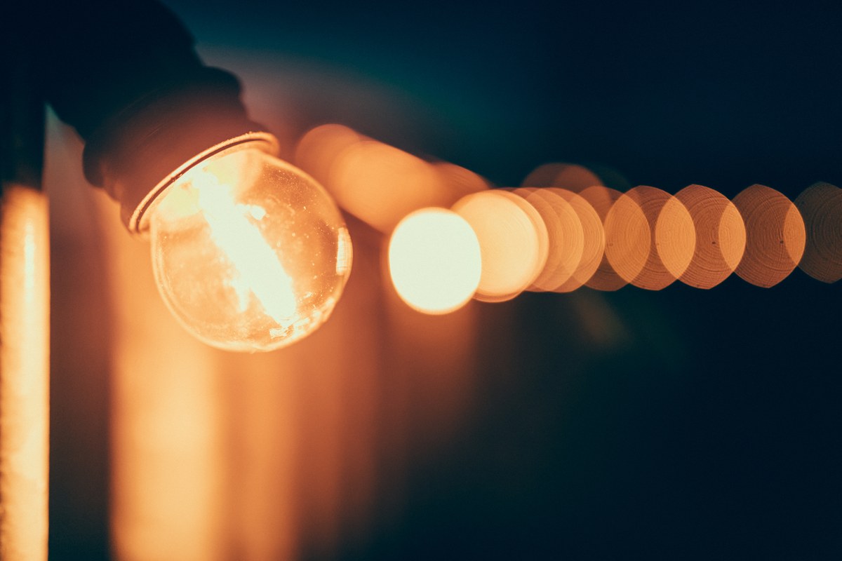 Close-up of a glowing festoon bulb with warm lights softly blurred behind it