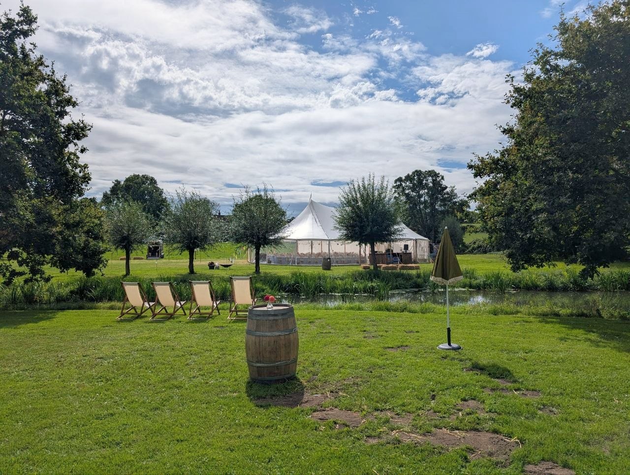 Four wooden deckchairs on a riverside lawn with the wedding marquee in the background near Frome