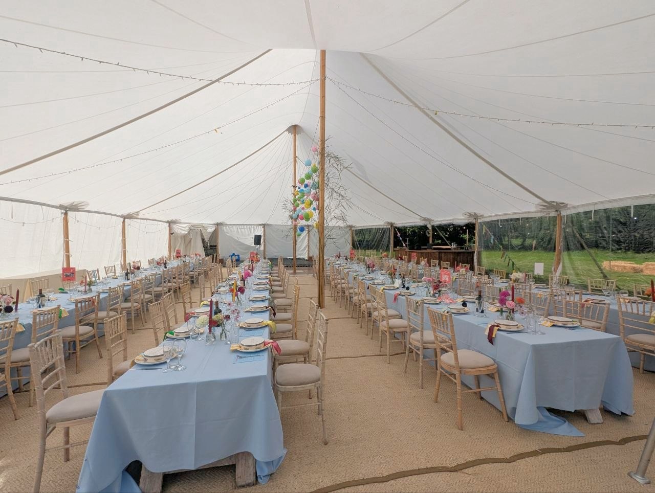 Wedding marquee interior with long dining tables, pale blue tablecloths, flowers and overhead lights