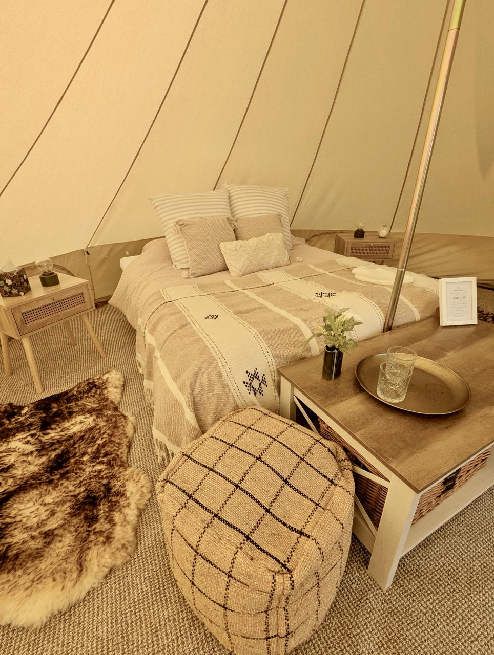 Furnished Camp Chic guest bell tent bed with neutral bedding, cushions, side tables and woven flooring for Ellie and Phil's Spargrove wedding
