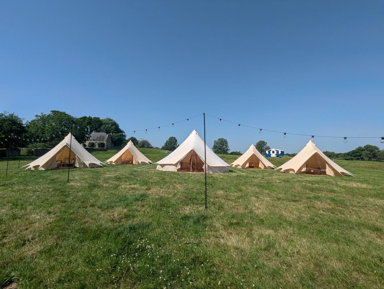 Camp Chic bell tent wedding glamping village on grass with festoon lights for Ellie and Phil's Spargrove wedding