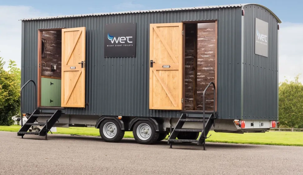 W.E.T. Hire branded shepherd’s-hut-style toilet trailer with open doors and access steps